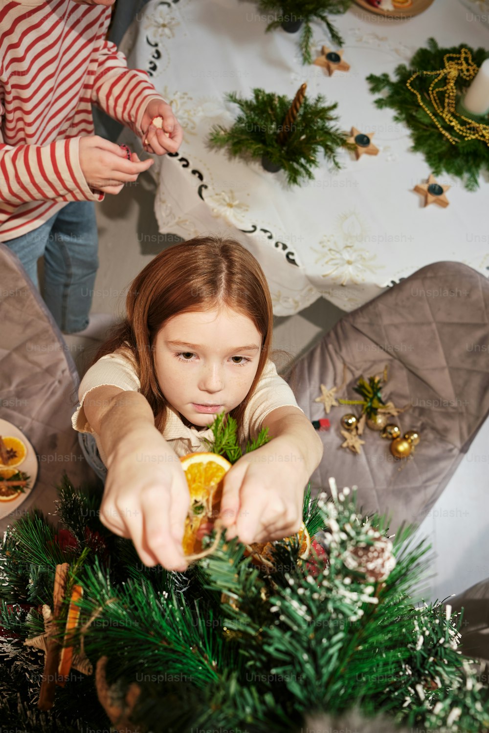 a little girl putting a piece of orange in a christmas wreath