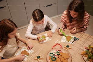 three girls sitting at a table making gingerbreads