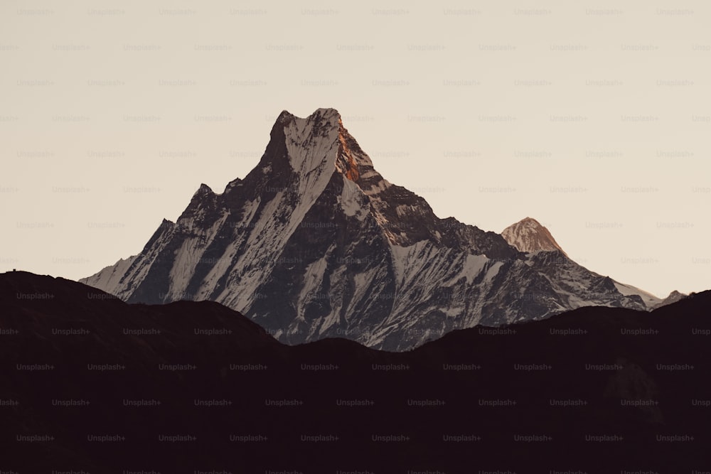 the top of a mountain is silhouetted against a gray sky