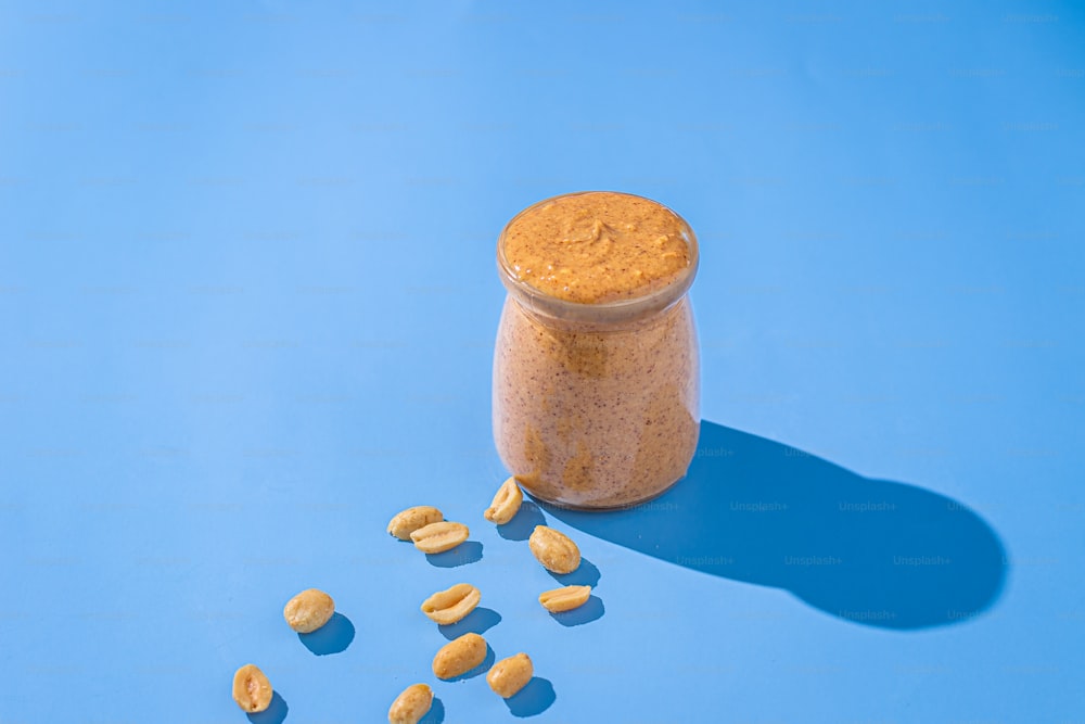 um frasco de manteiga de amendoim ao lado de amendoim em um fundo azul