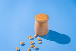 un frasco de mantequilla de maní junto a cacahuetes sobre un fondo azul