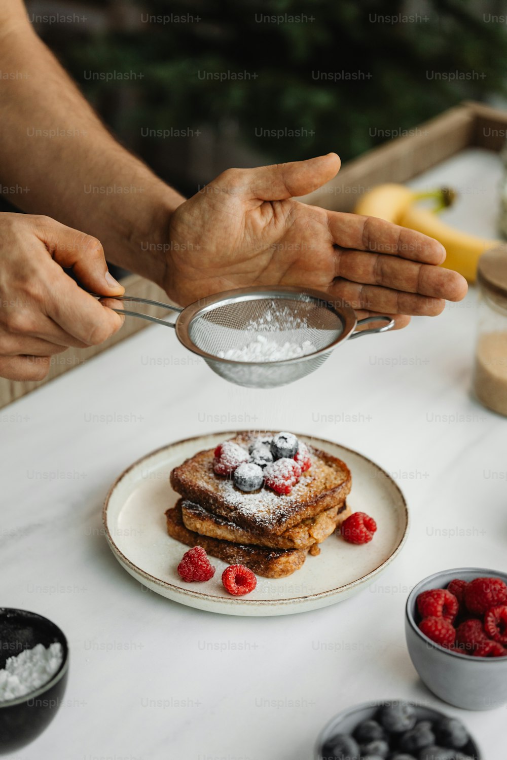 Eine Person, die Zucker auf einen Teller mit French Toast gießt