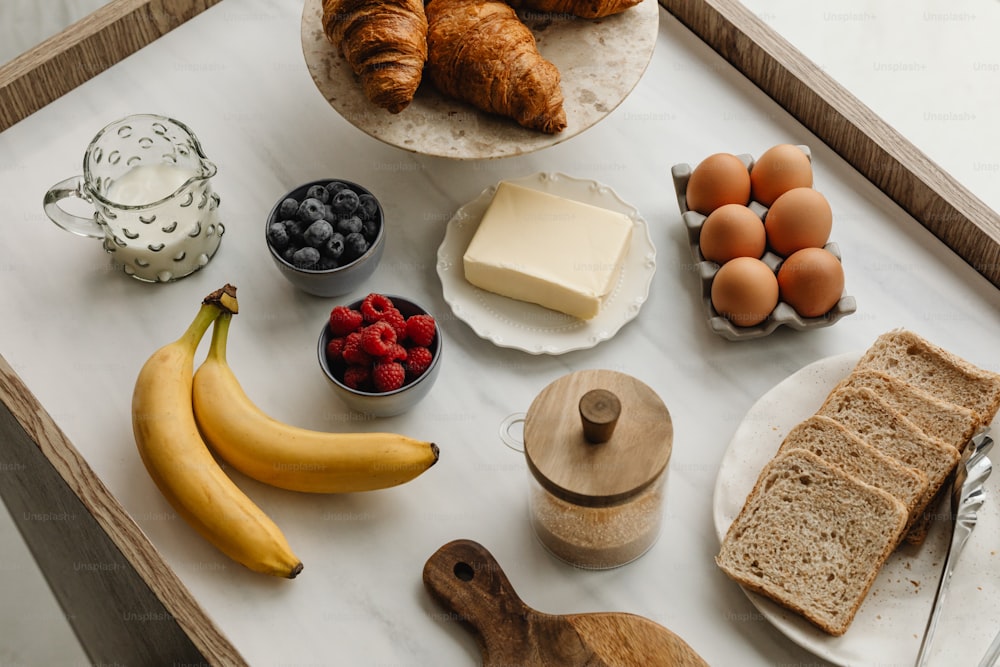 a tray with bread, fruit, butter, and croissants