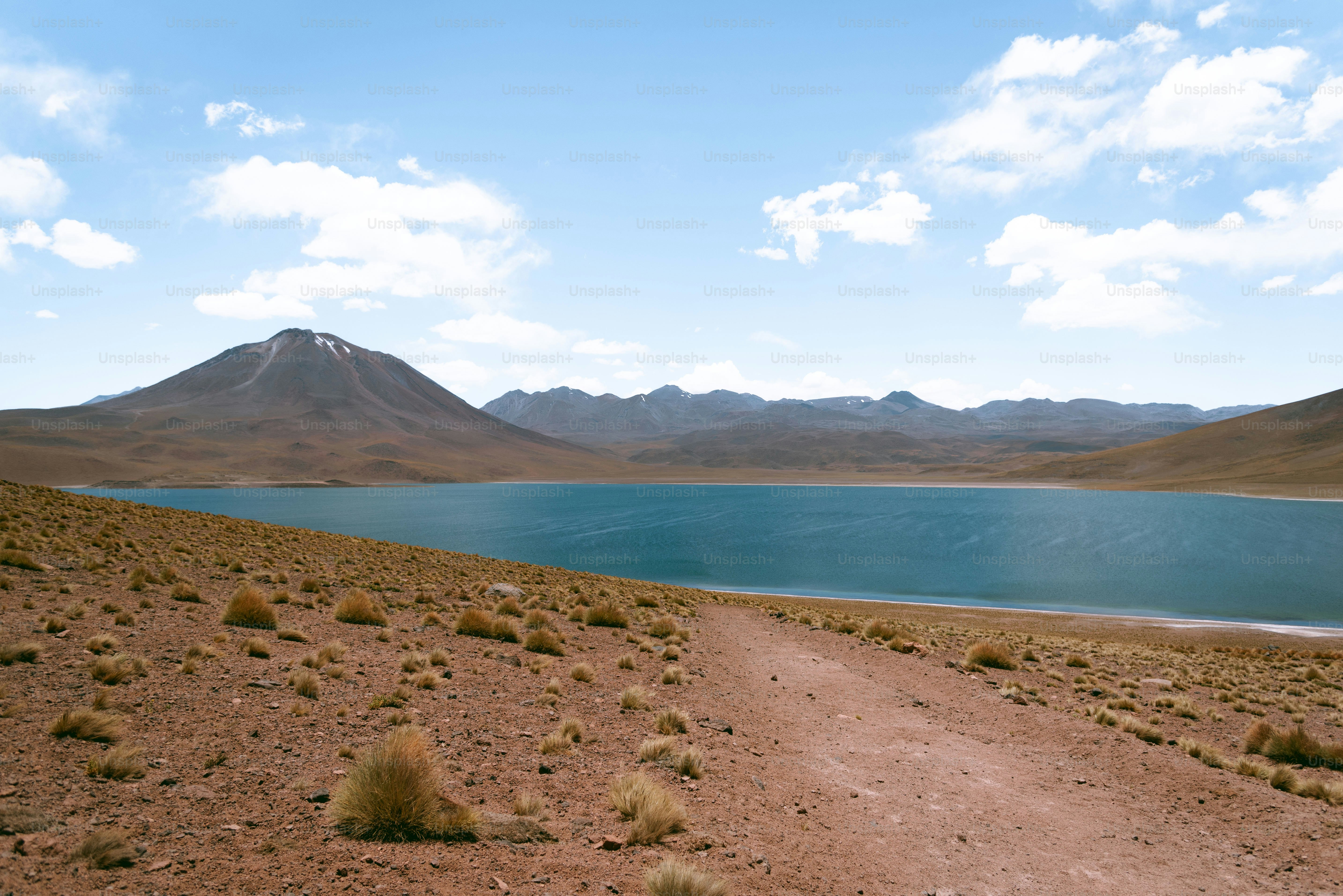 a dirt road leading to a lake with mountains in the background