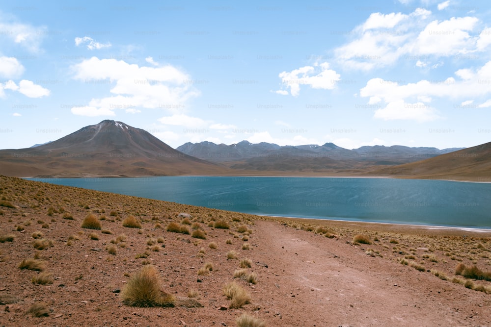 a dirt road leading to a lake with mountains in the background