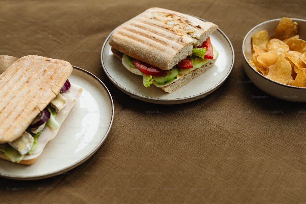 two plates with sandwiches and chips on a table