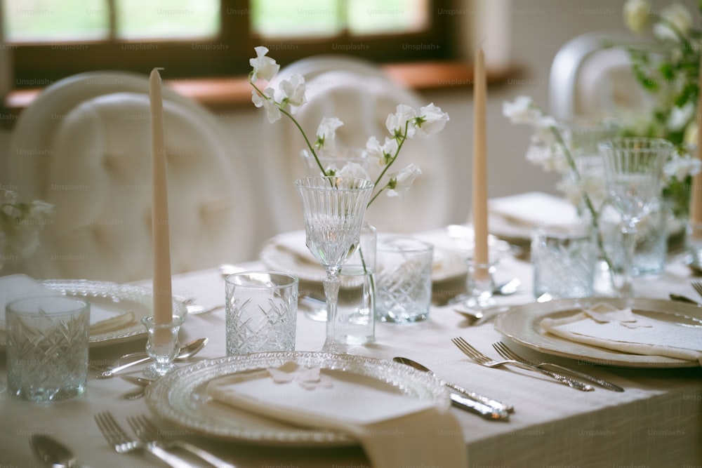 a table set for a formal dinner with flowers in a vase