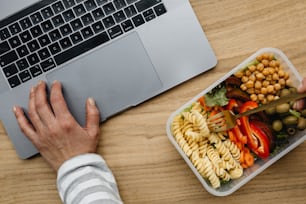 a person is using a laptop and eating pasta salad