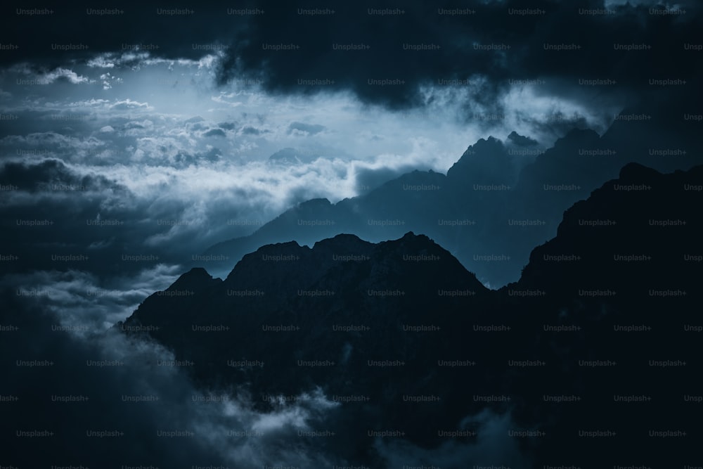 a dark sky with clouds and mountains in the foreground