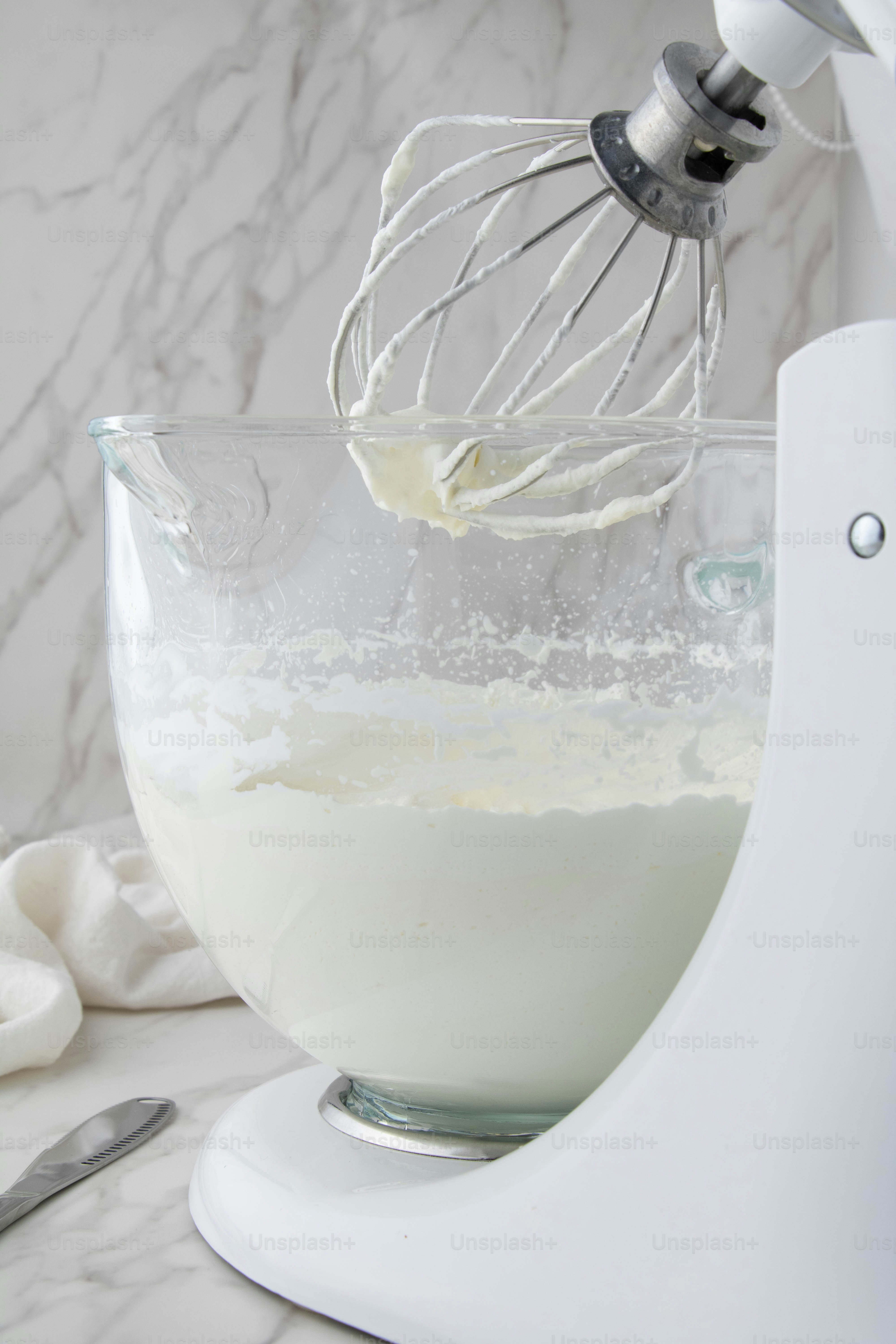 a whisk in a glass bowl next to a mixer