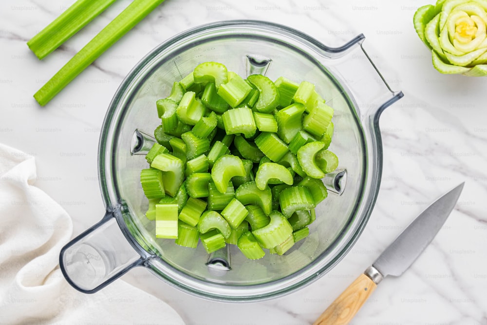 a glass bowl filled with chopped celery next to a knife