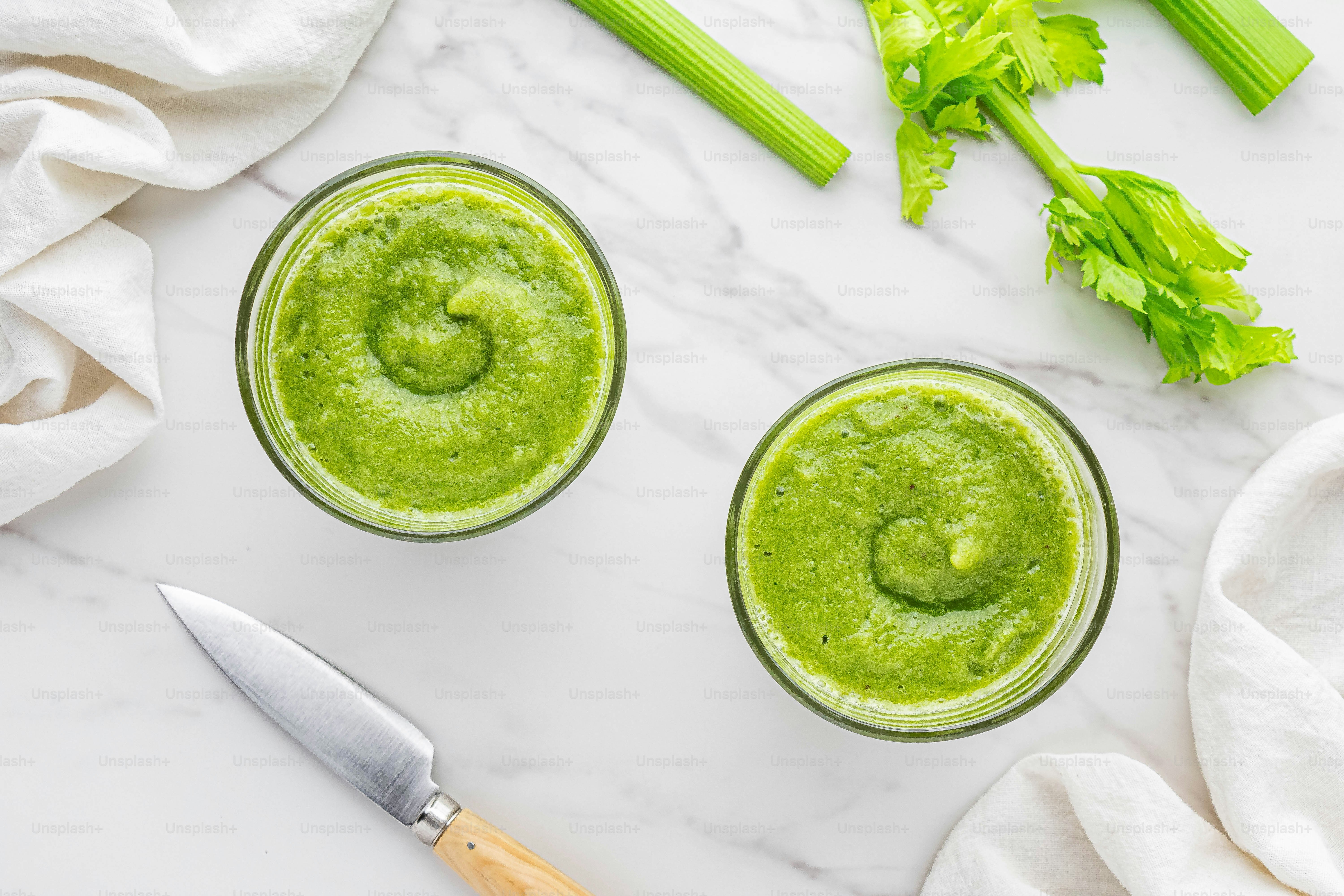 two glasses of green smoothie with celery on the side