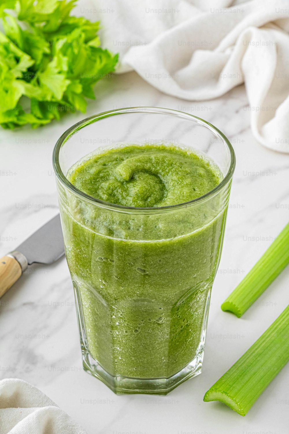 a glass filled with green liquid next to celery stalks