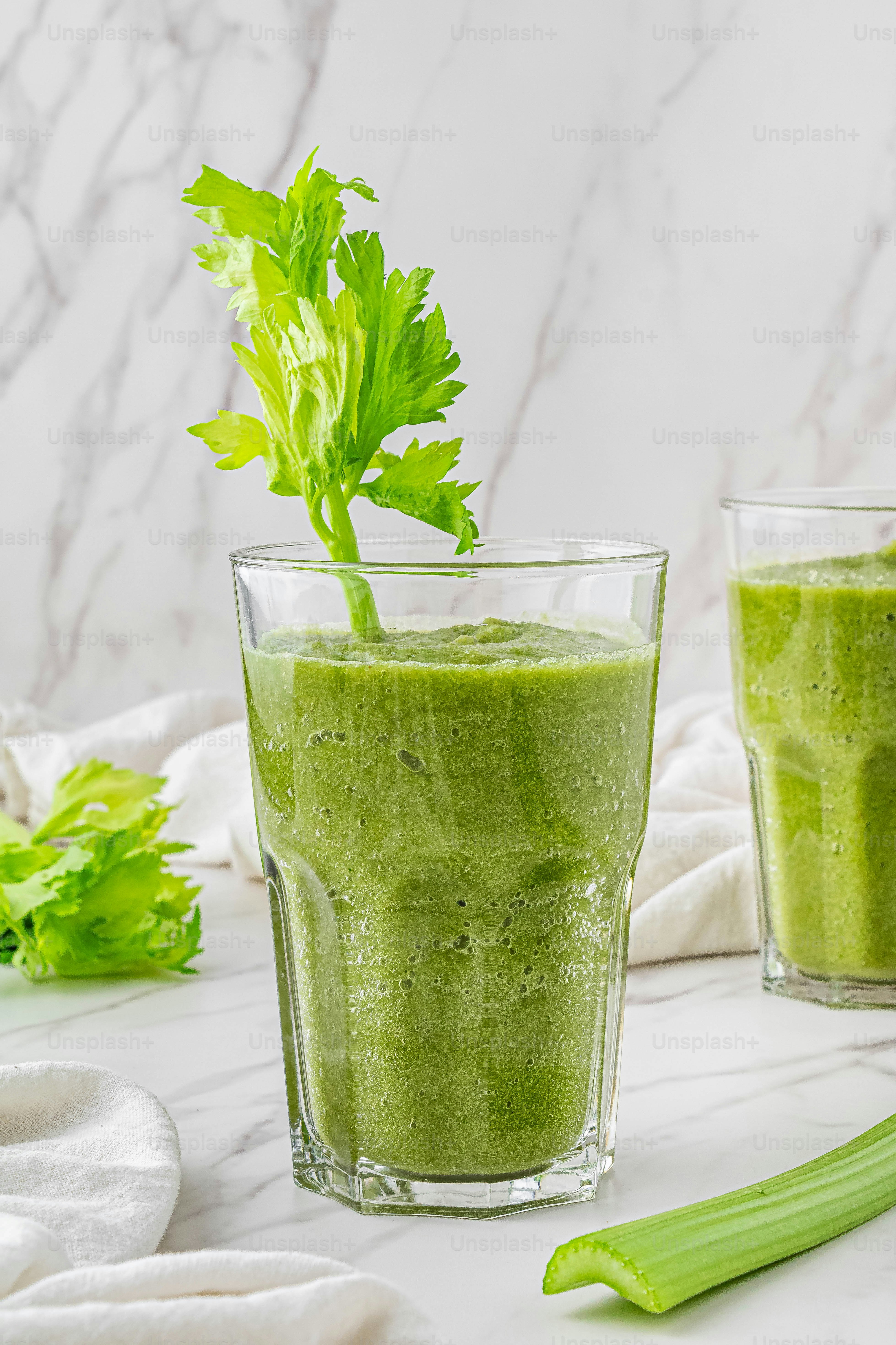 Dos vasos de batido verde con una guarnición de hojas verdes