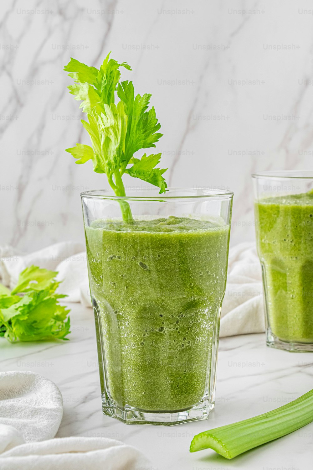 two glasses of green smoothie with a green leafy garnish