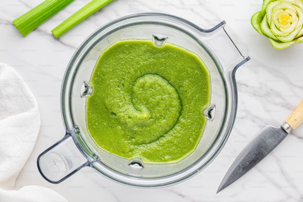 a blender filled with green liquid next to celery stalks