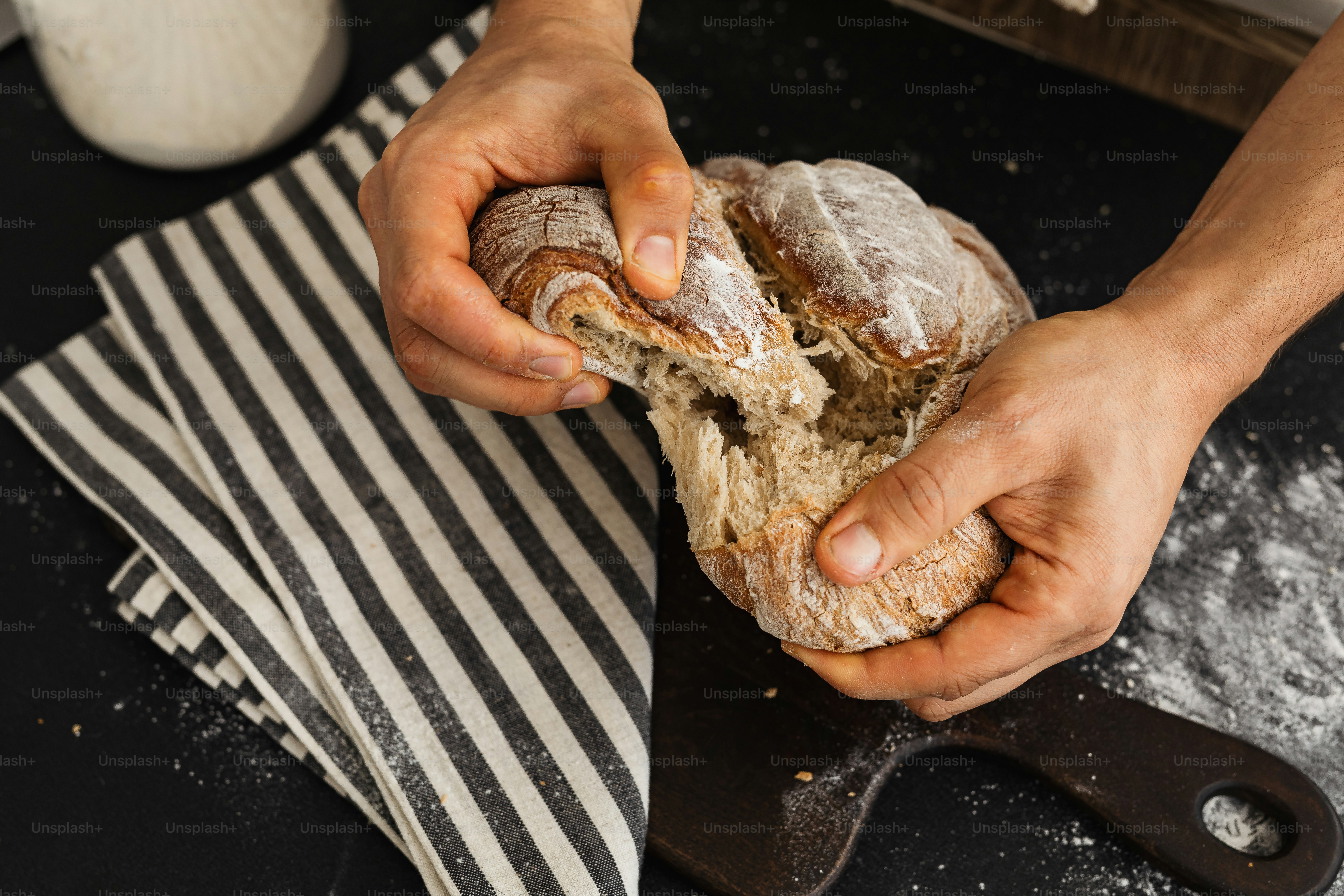 Hands breaking apart a rustic loaf of bread.