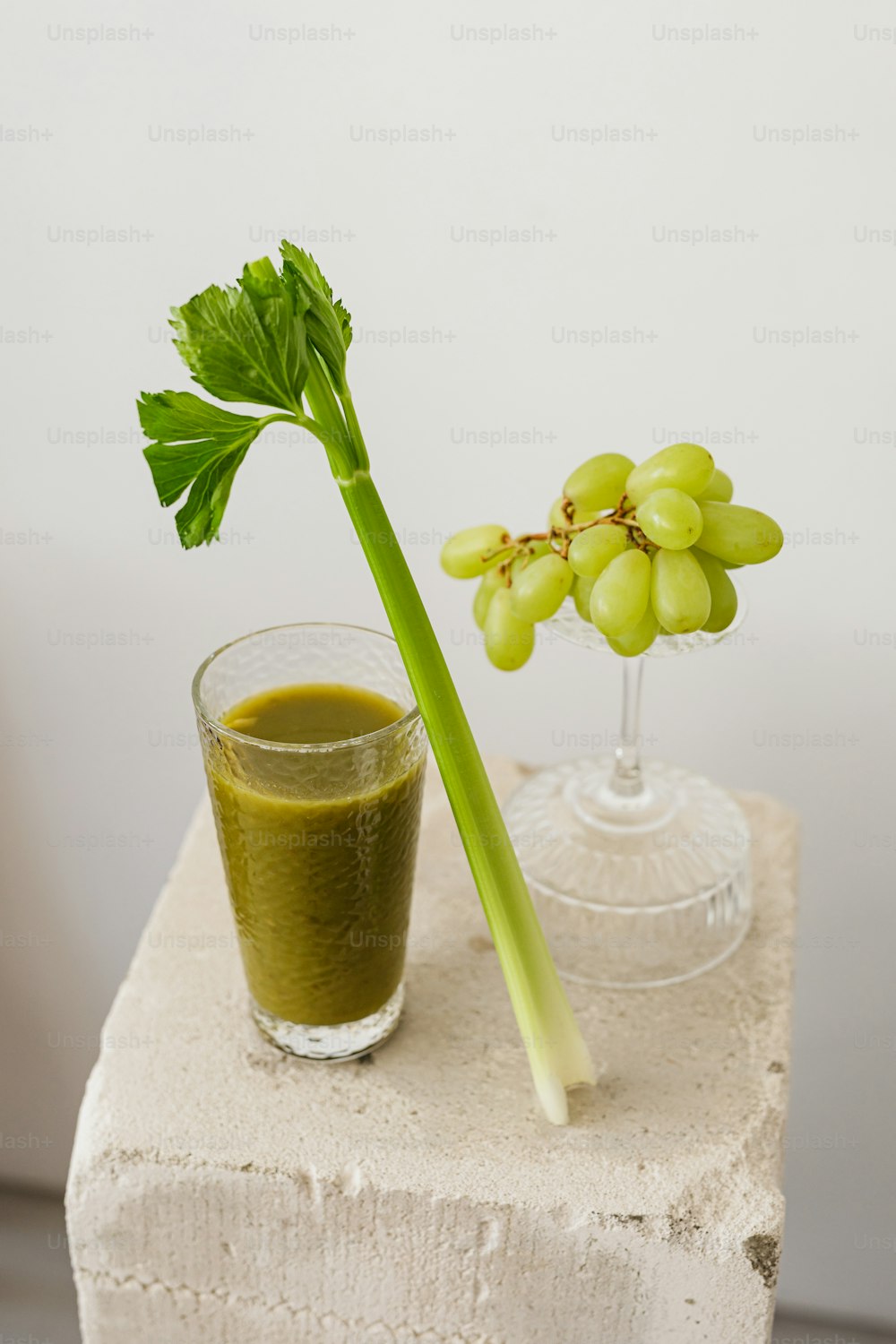 a glass of green juice next to a stem of grapes