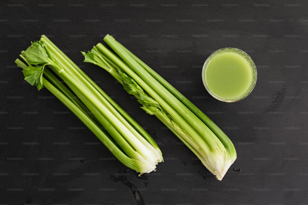 celery and a glass of green juice on a black surface