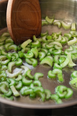 a wooden spoon stirring a pot filled with green vegetables