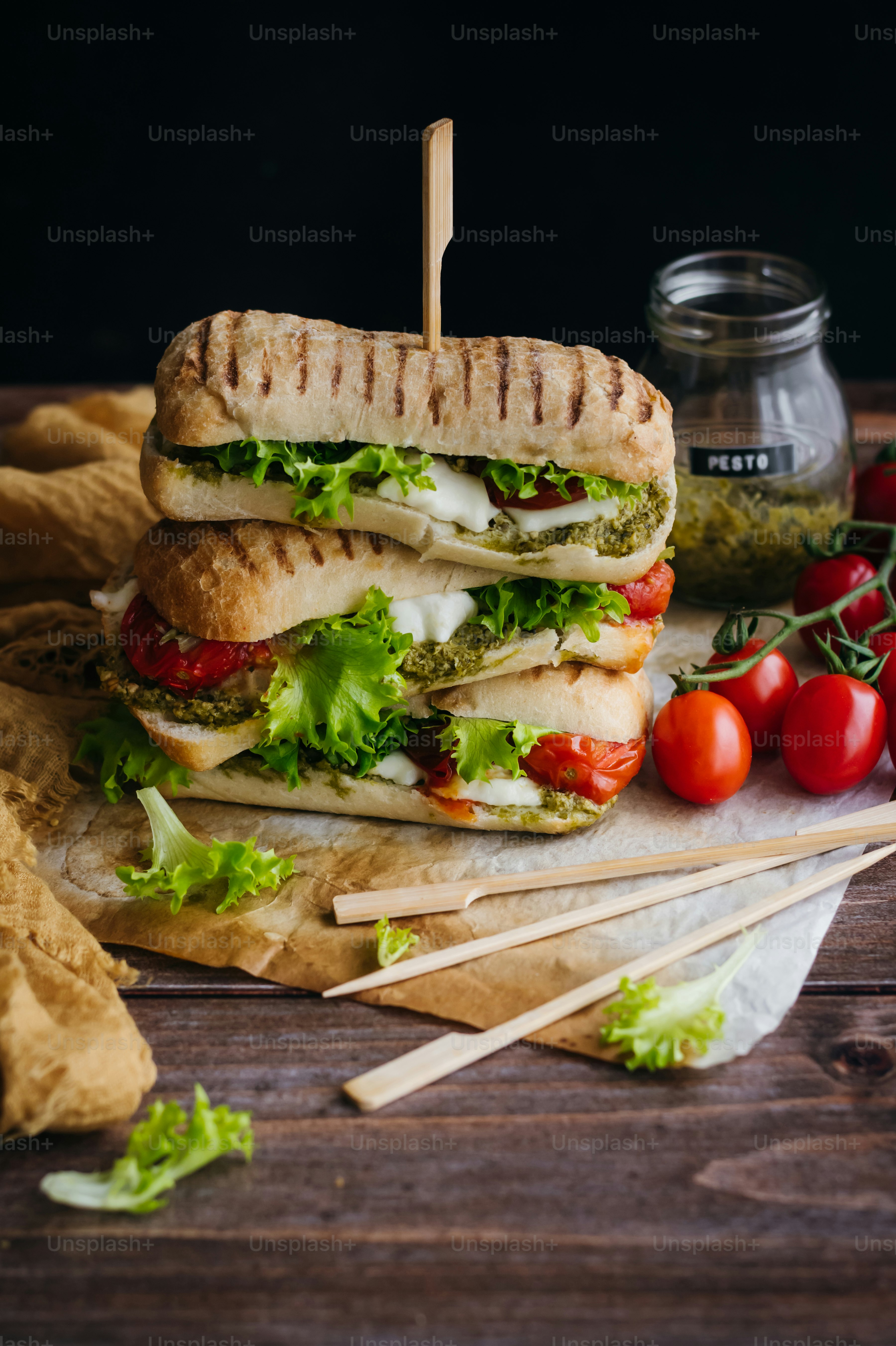 a sandwich with lettuce, tomato, and pesto on a cutting board