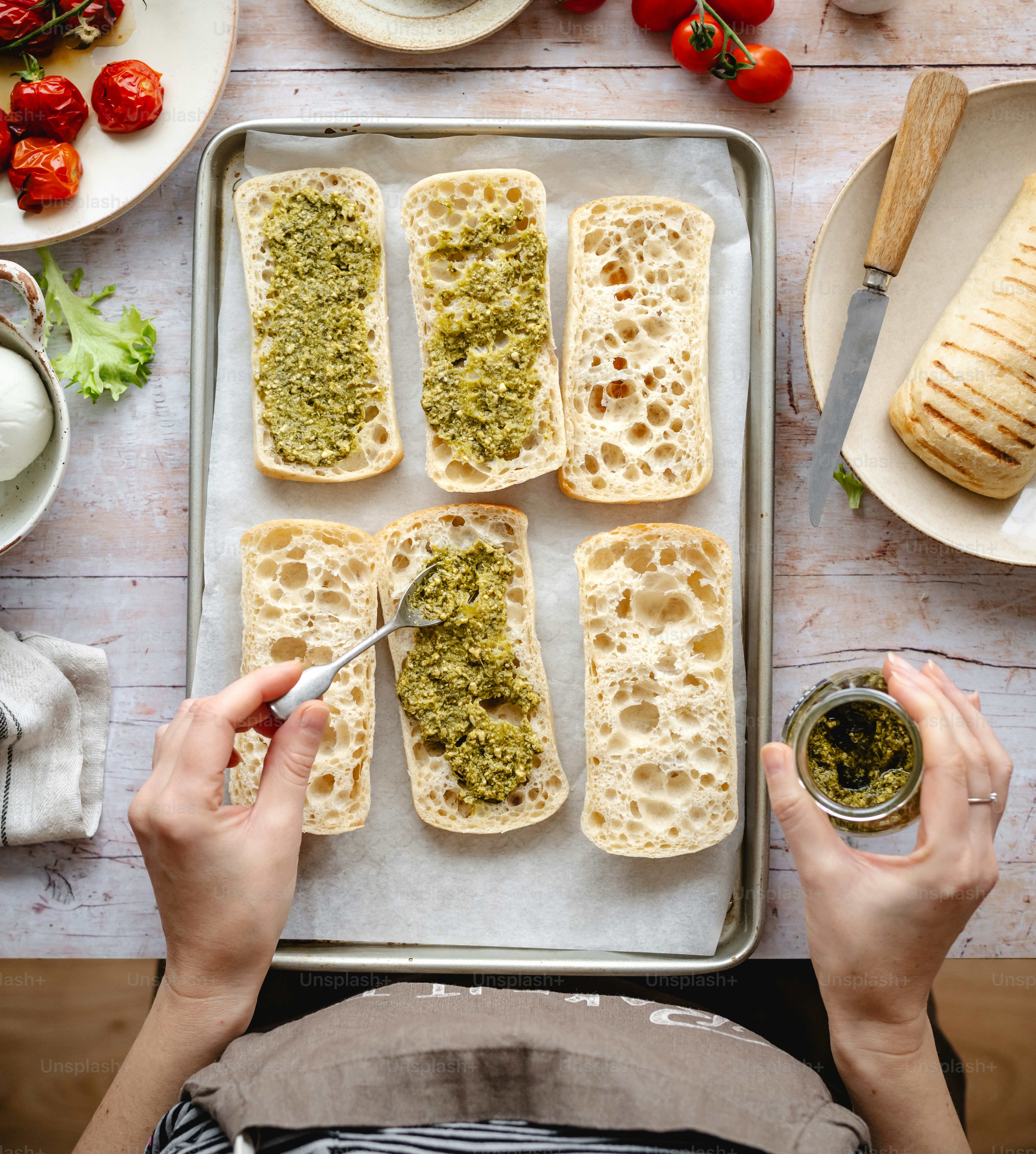 a person spreading pesto on bread on a pan