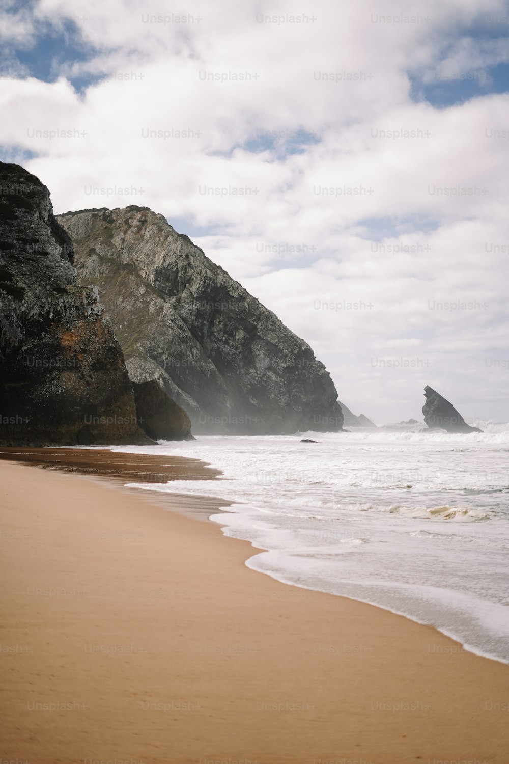 a sandy beach next to a large rock formation