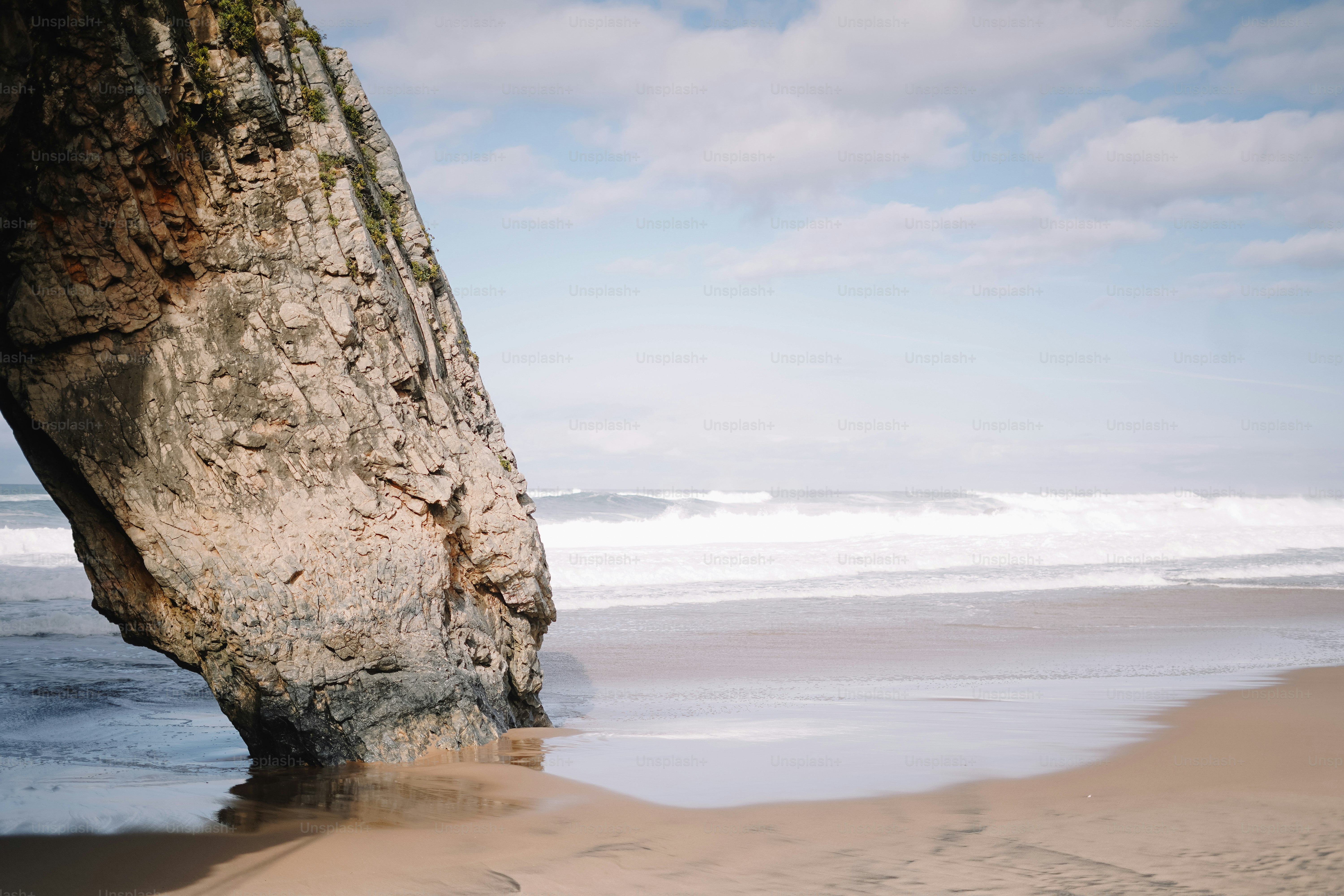 A sandy beach next to a large rock formation photo – Portugal Image on ...