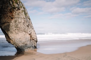 un gros rocher qui sort du sable de la plage