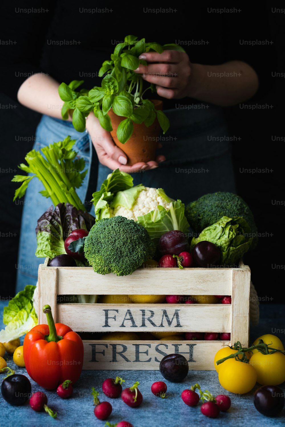 a person holding a potted plant over a crate of vegetables