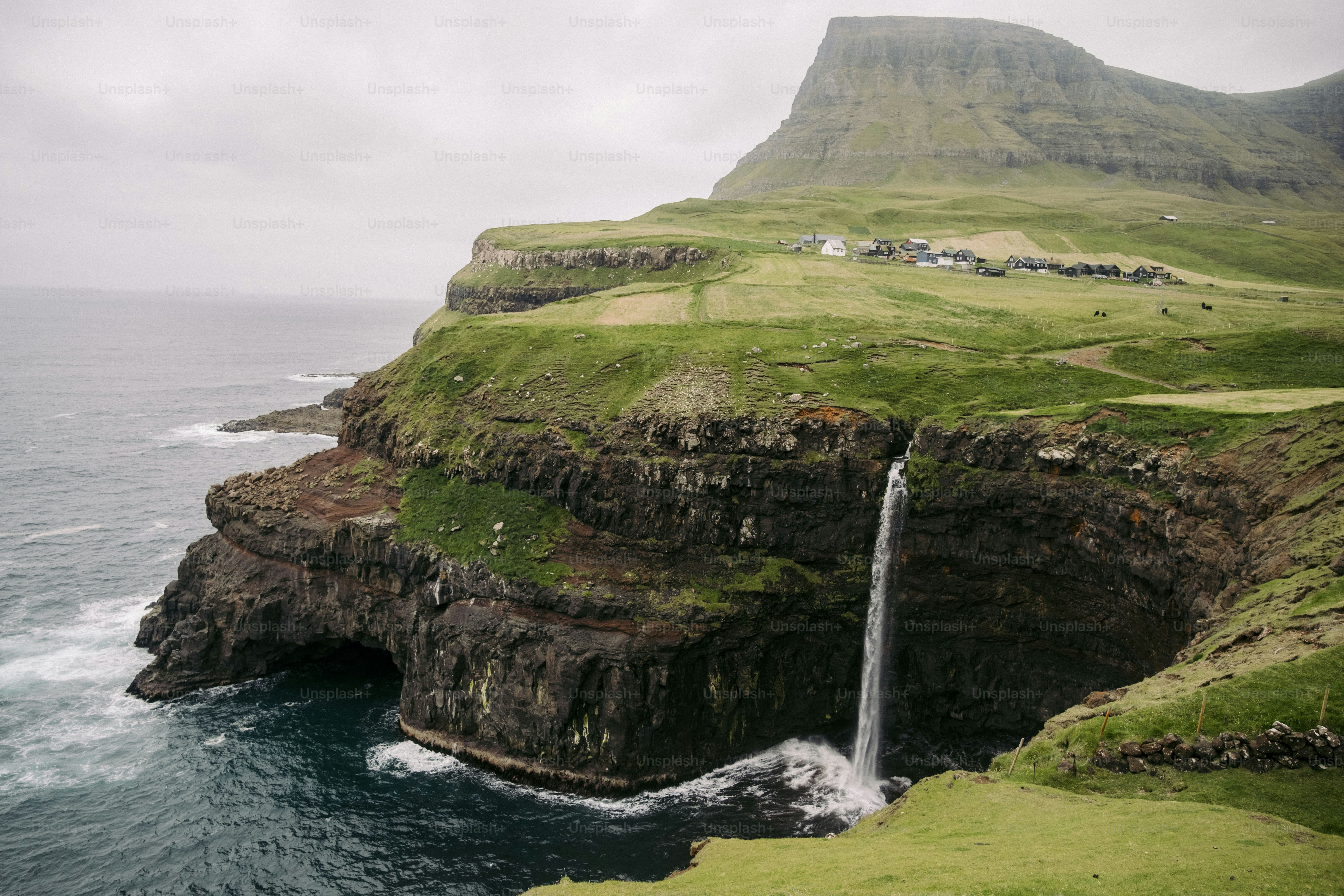A waterfall is coming out of a cliff into the ocean photo – Faroe ...