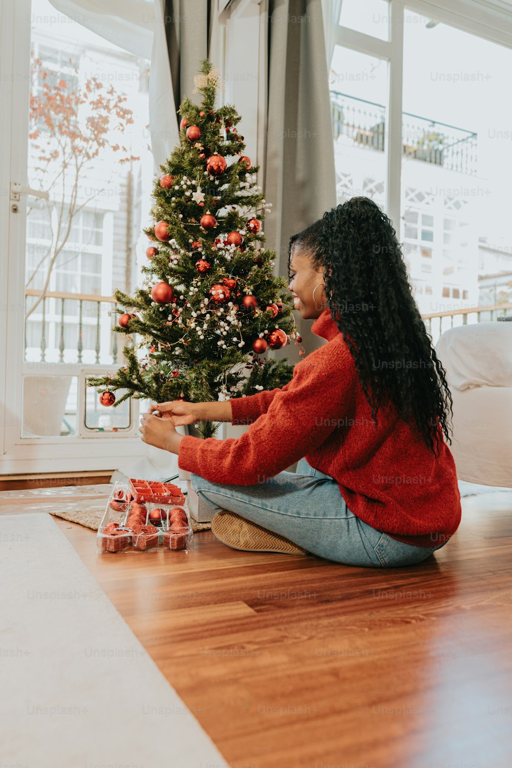 a woman sitting on the floor next to a christmas tree