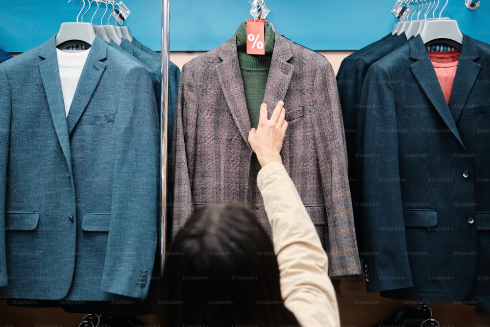 a person reaching for a suit on a rack