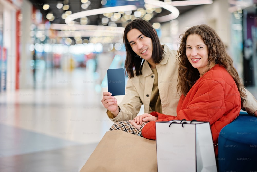 a man and a woman sitting on a bench holding shopping bags and a cell phone
