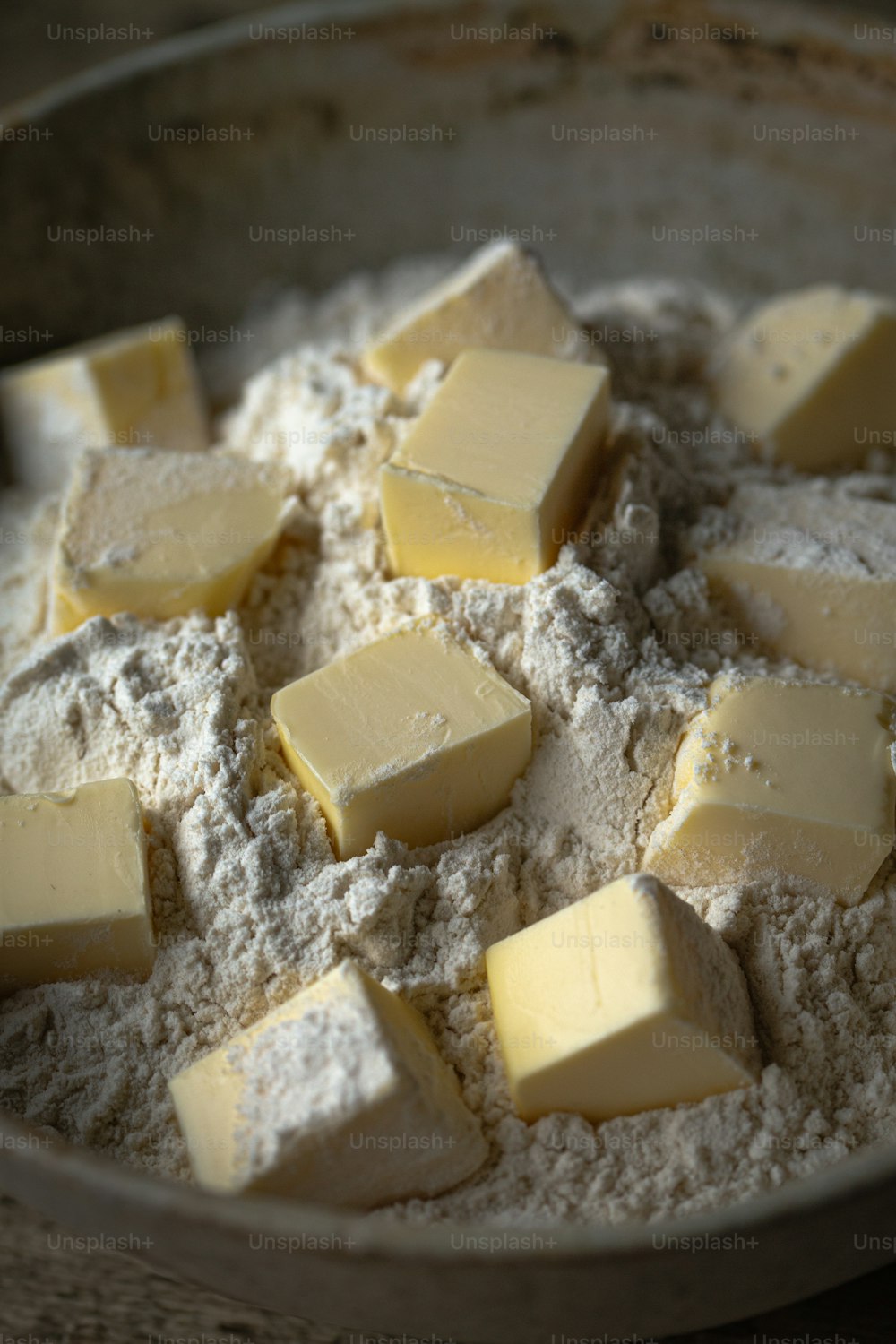 a bowl of flour with cubes of butter on top