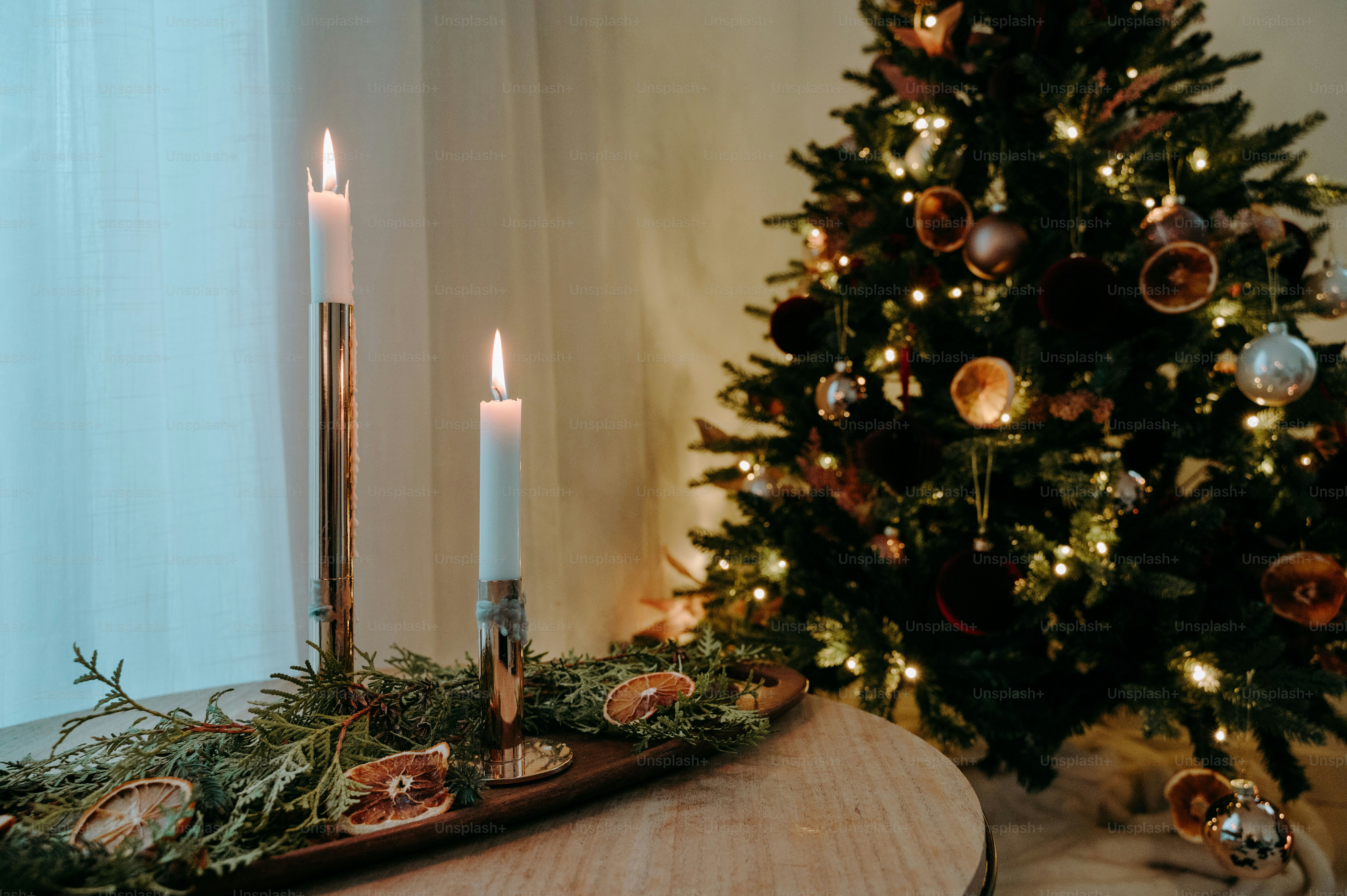 Una candela accesa su un tavolo accanto a un albero di Natale