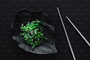 a black plate topped with green vegetables next to chopsticks