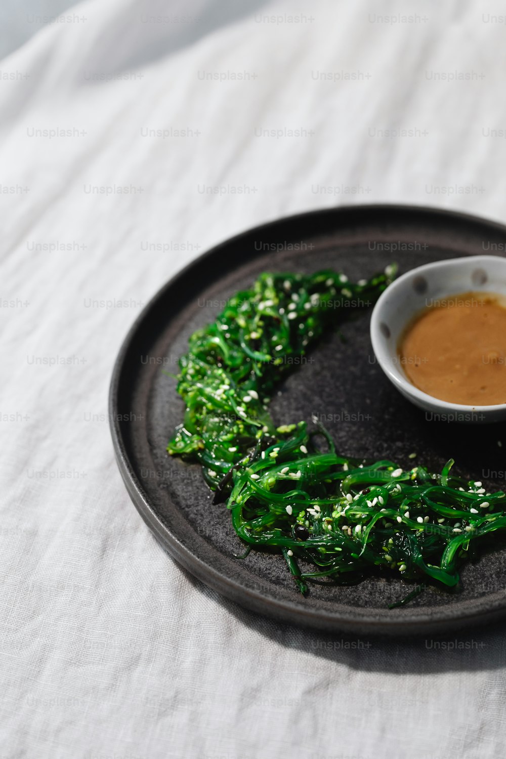 un plato negro cubierto con verduras y un tazón de salsa para mojar