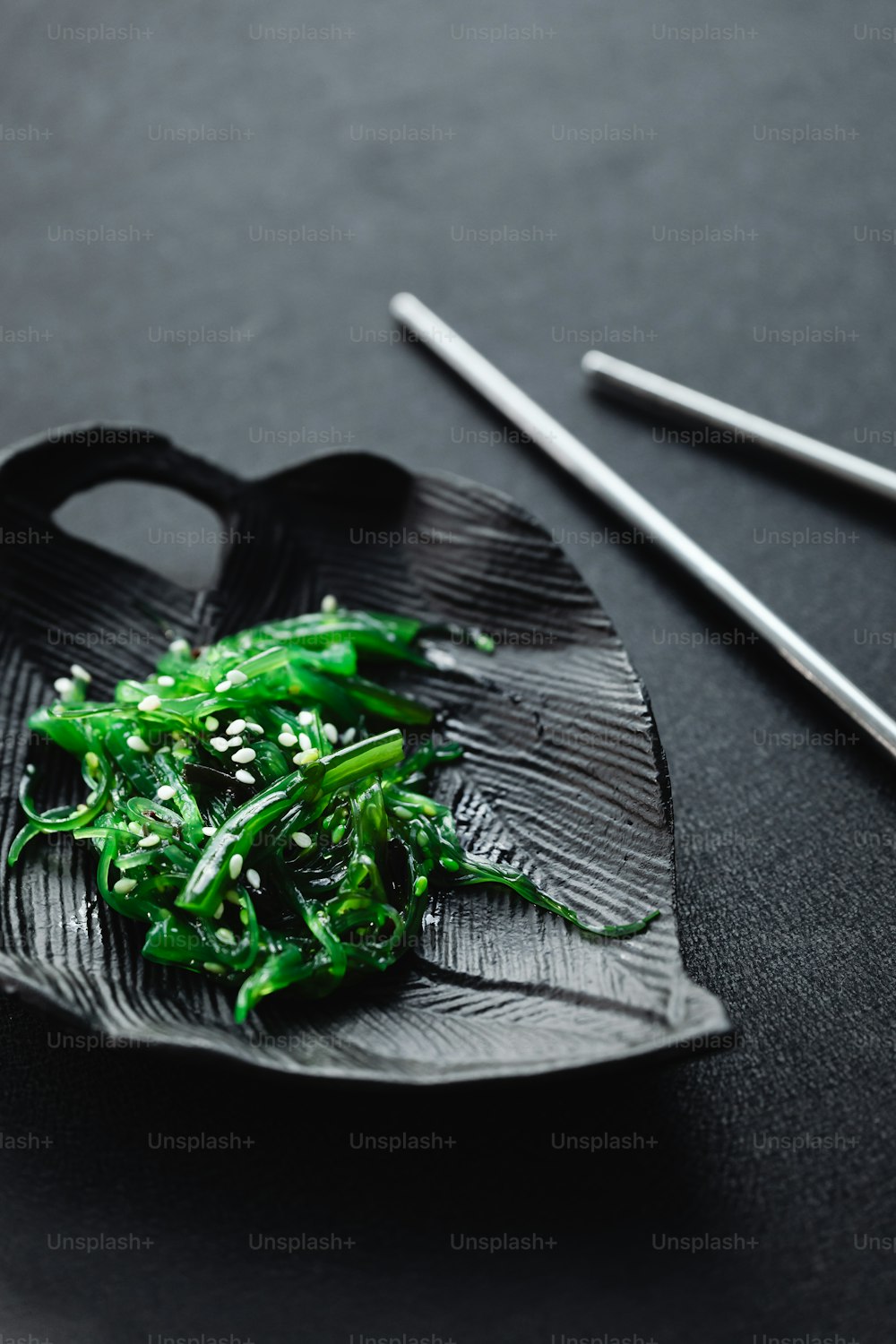 a black plate topped with green vegetables and chopsticks