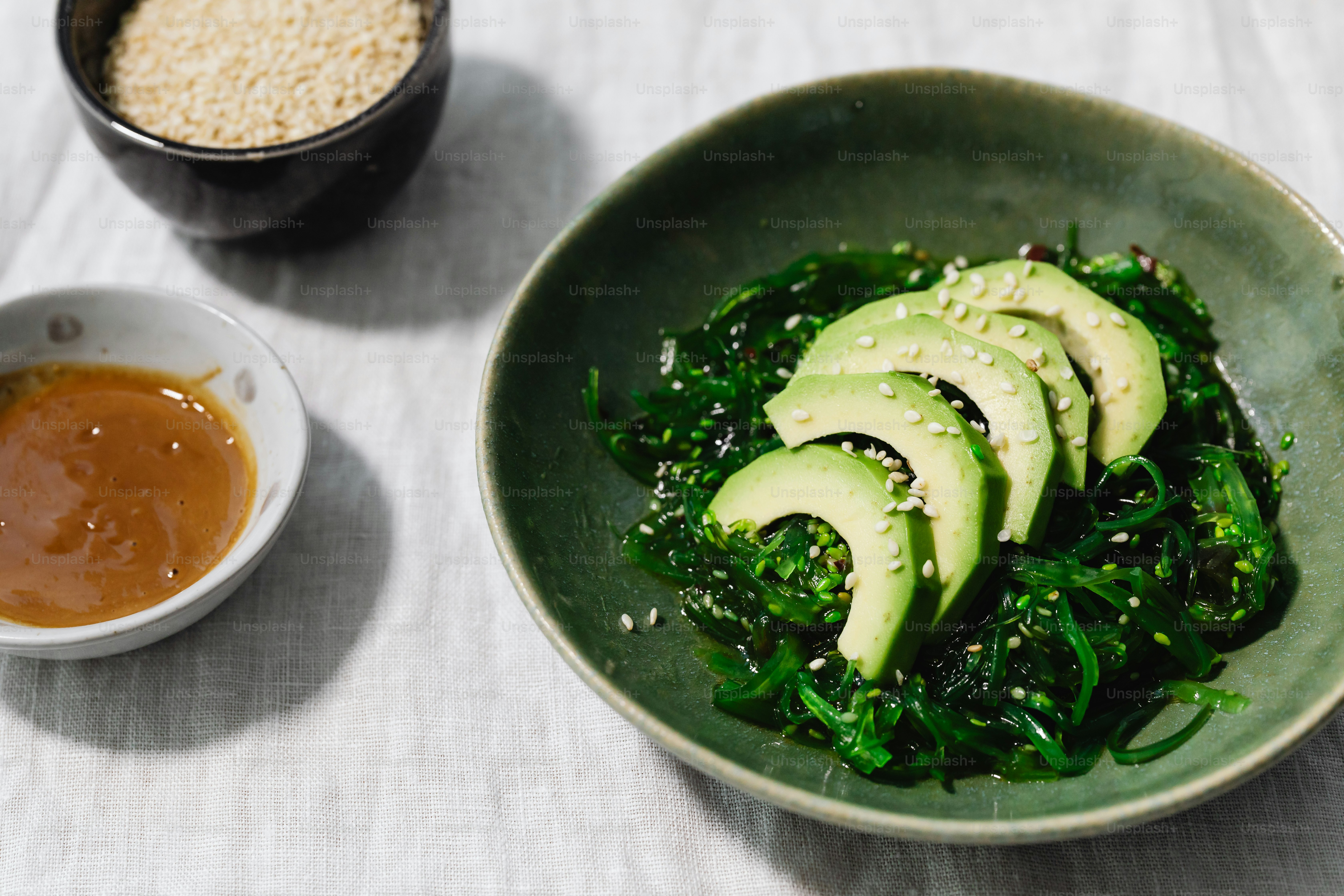 a green bowl with sliced avocados and sesame seeds