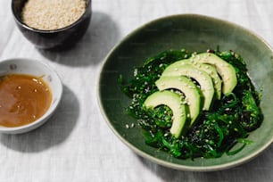 a green bowl with sliced avocados and sesame seeds