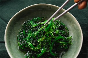 a bowl of green vegetables with chopsticks in it