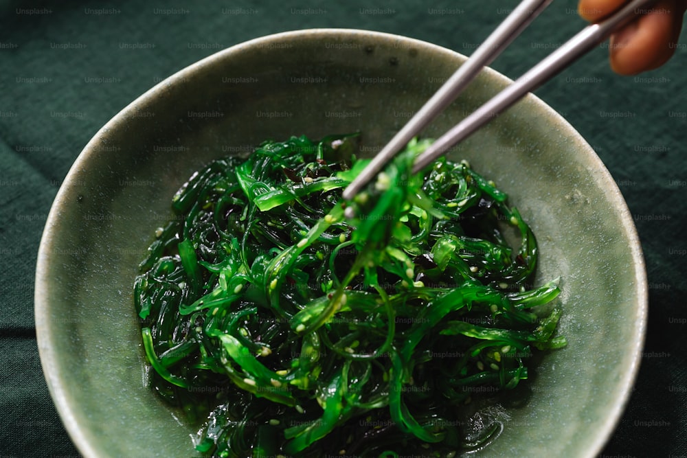 a bowl of green vegetables with chopsticks in it