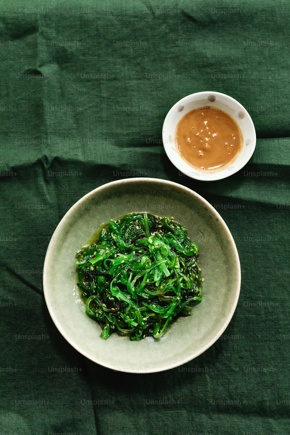 a white bowl filled with greens next to a bowl of sauce