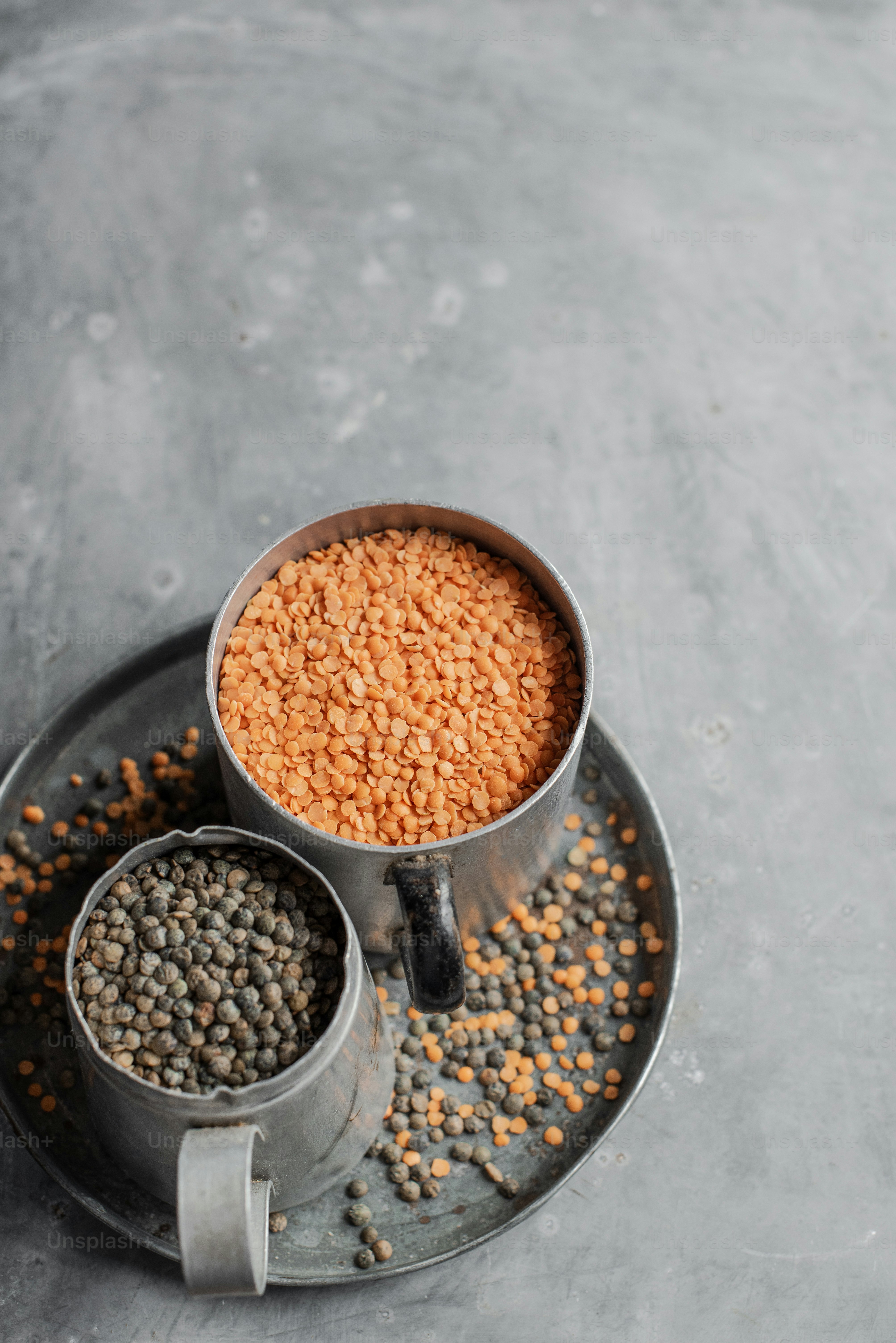 Red, green and brown lentils in a metal cups on a metal plate on a grey background.