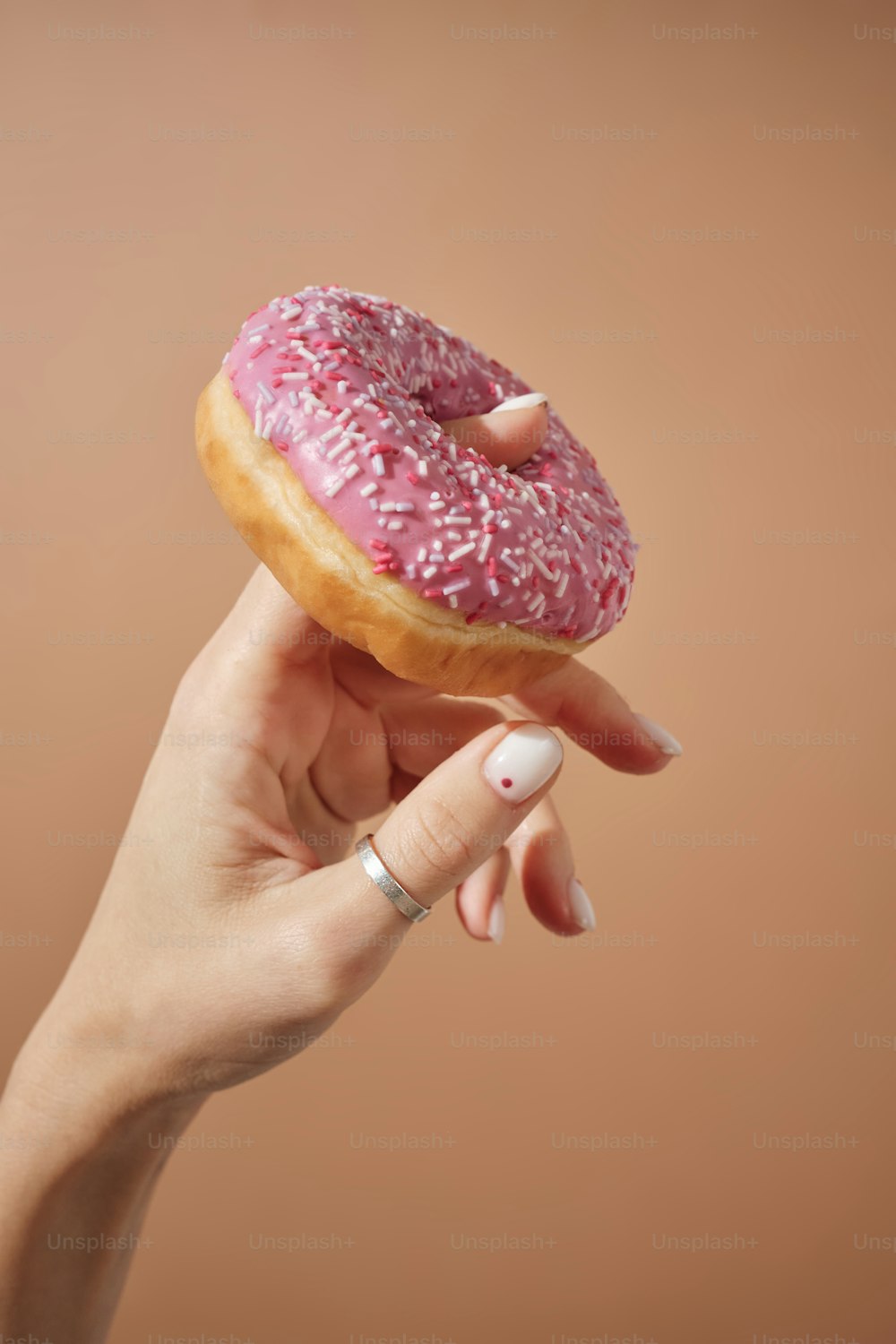 a hand holding a pink donut with sprinkles