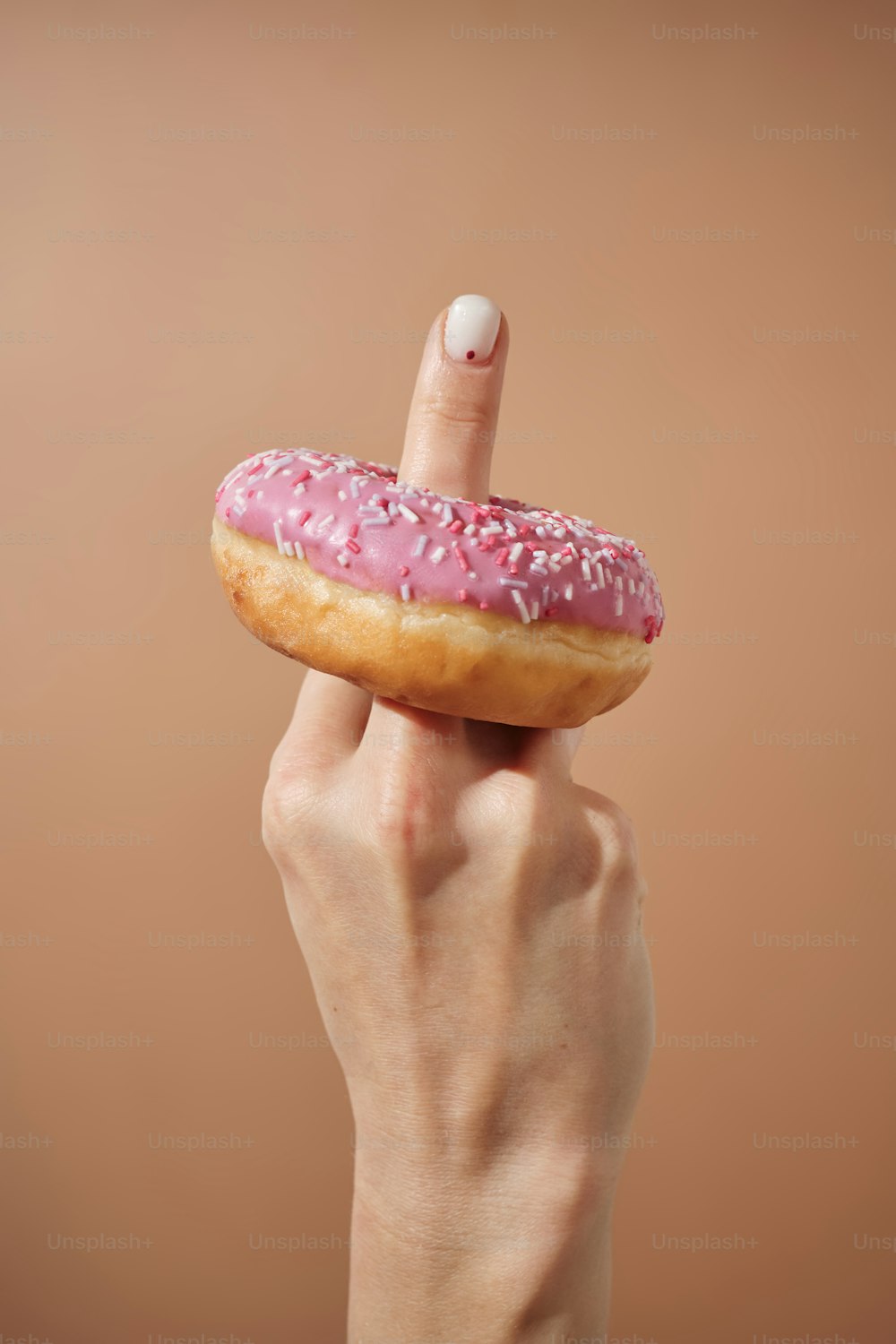 a hand holding a doughnut with pink icing and sprinkles