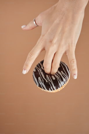 a woman's hand reaching for a donut with chocolate icing