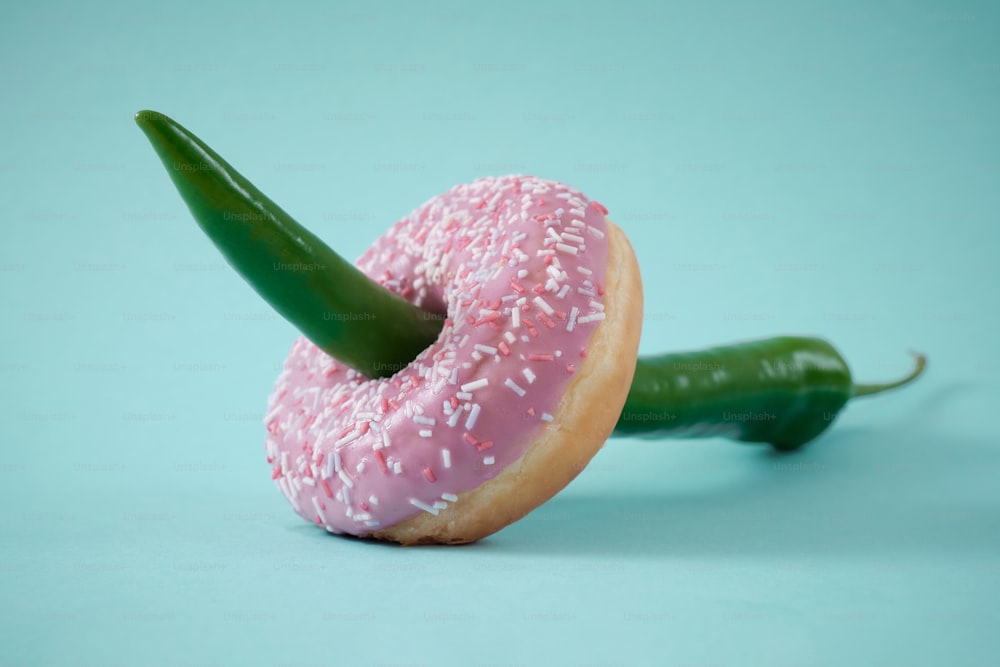 a pink donut with sprinkles and a green pepper