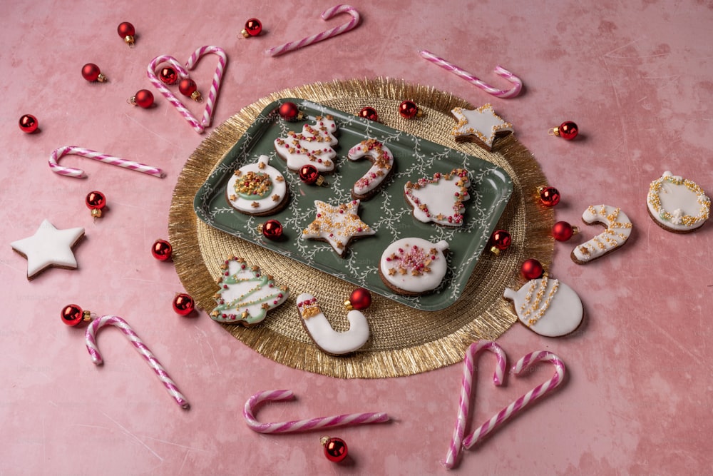 uma bandeja de biscoitos e bengalas de doces em uma superfície rosa